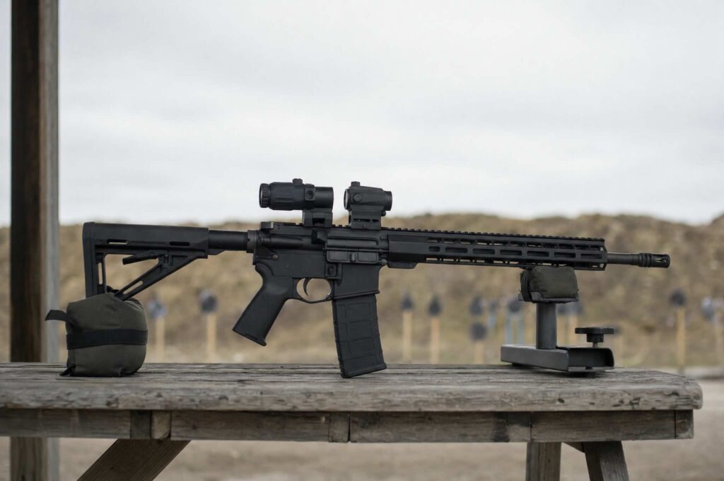 AR-15 with a red dot and flip-to-side magnifier resting on a range bench